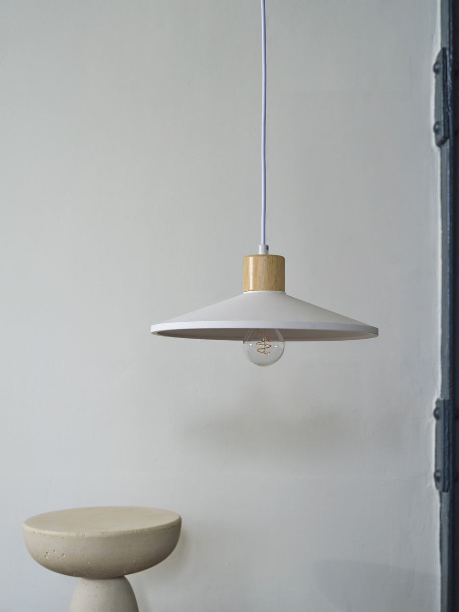 Suspension blanche éclairée, ampoule apparente, devant un mur neutre et un tabouret béton.