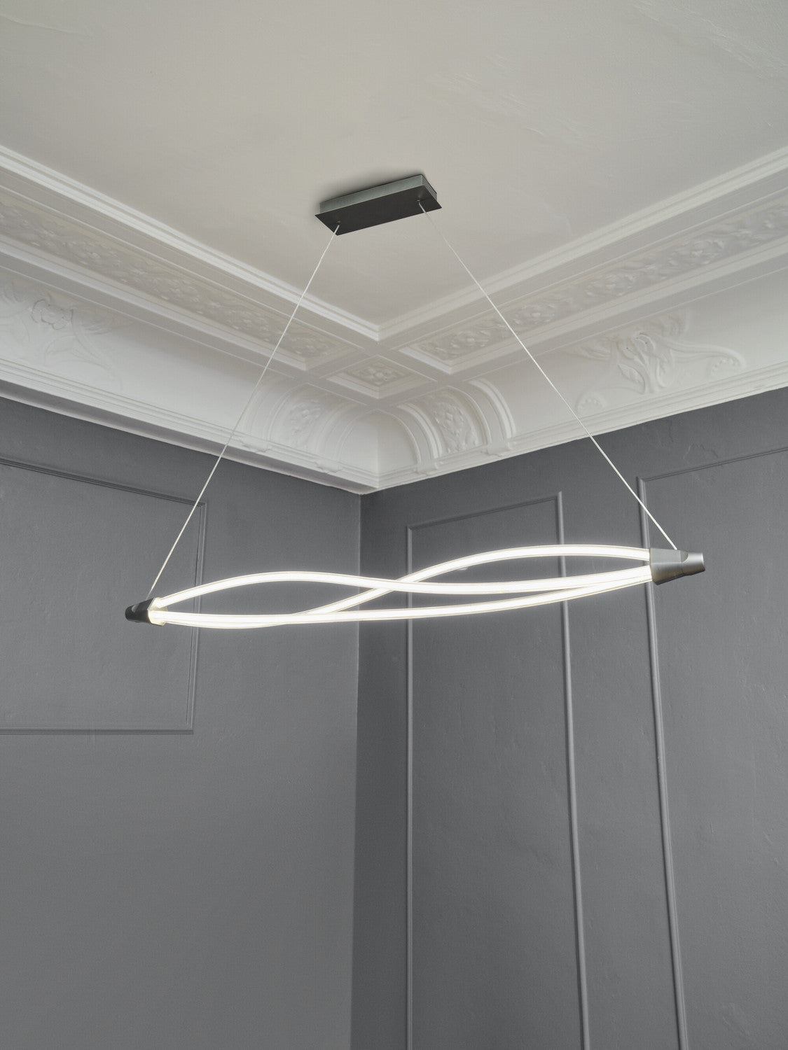 Vue en intérieur de la suspension allumée sous moulures, câbles et fixation plafond visibles.