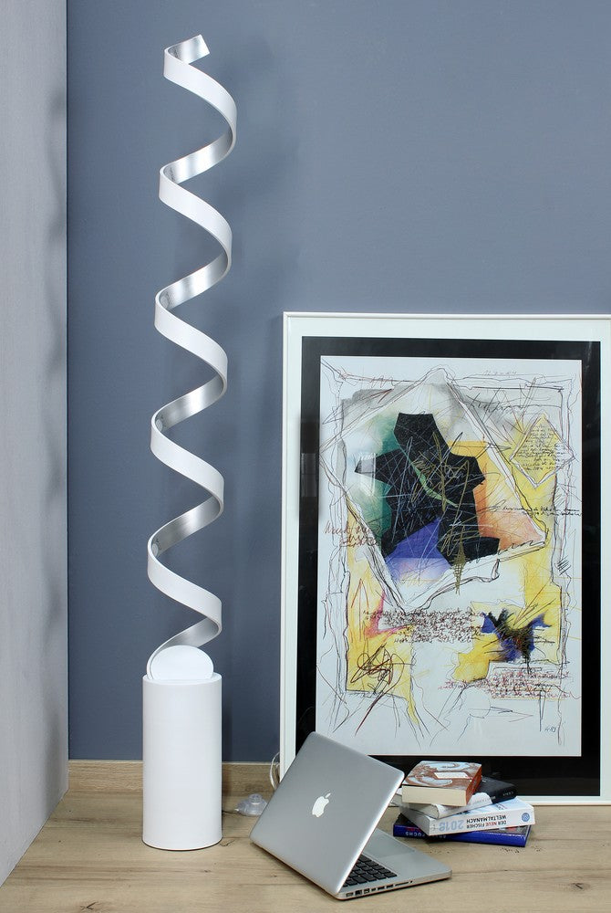 Vue d'ambiance : lampadaire spiralé blanc non allumé devant mur gris, avec cadre et ordinateur.