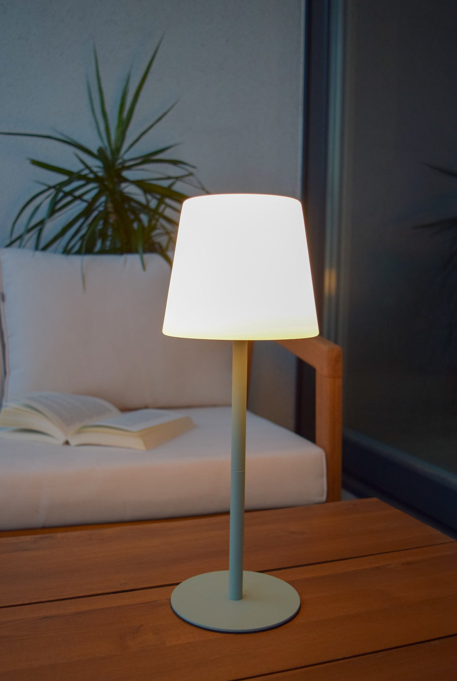 Ambiance terrasse, lampe allumée sur table en bois devant un fauteuil blanc