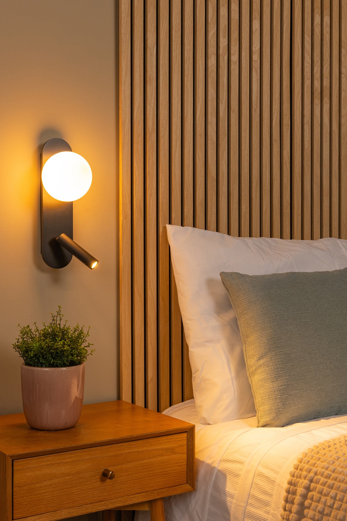 Mise en ambiance chaleureuse dans une chambre avec applique allumée près du lit.
