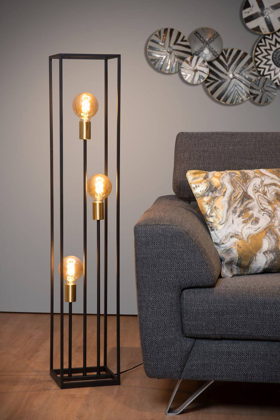 Gros plan du lampadaire illuminé à côté du canapé gris et coussin marbré
