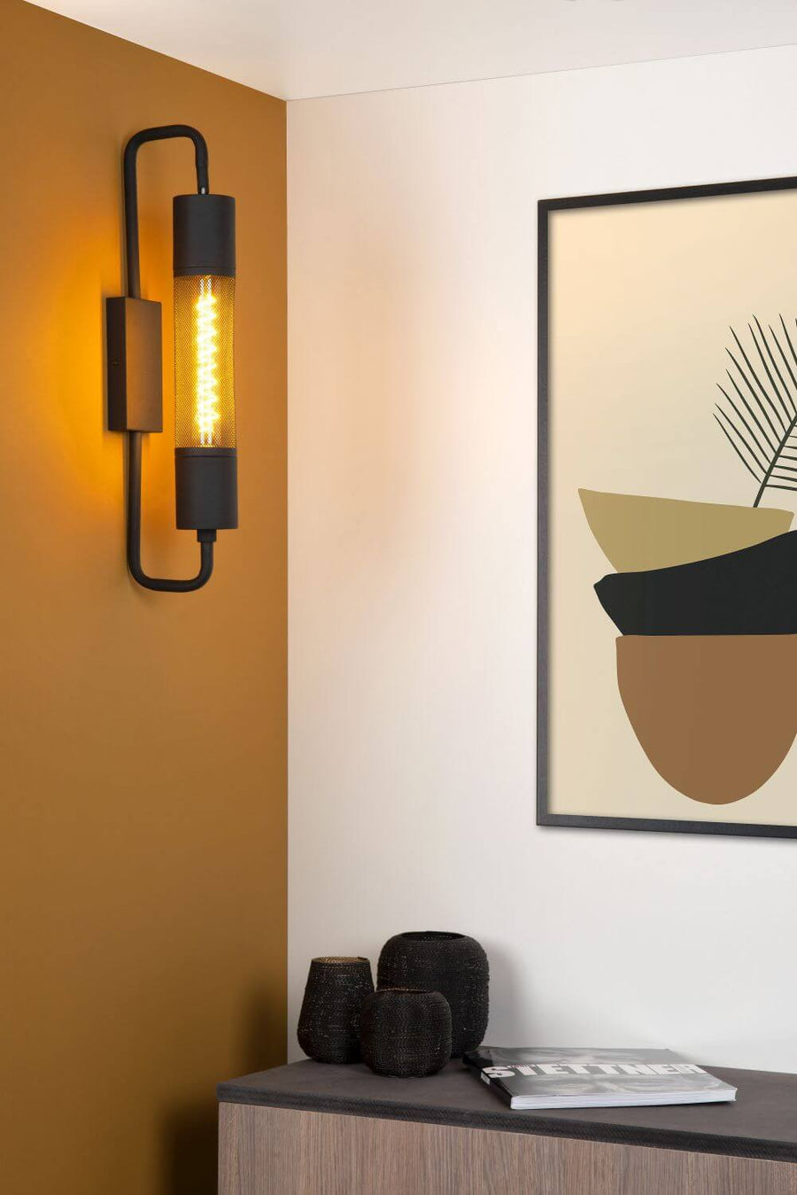 Vue rapprochée de l'applique murale noire allumée, fixée sur un mur ocre.