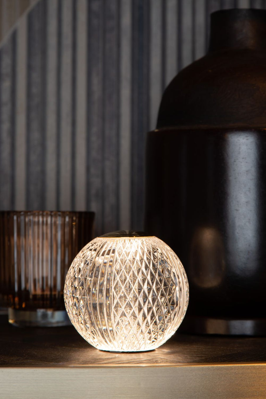 Lampe à poser allumée en verre transparent à motif losanges, capuchon doré mat, gros plan.