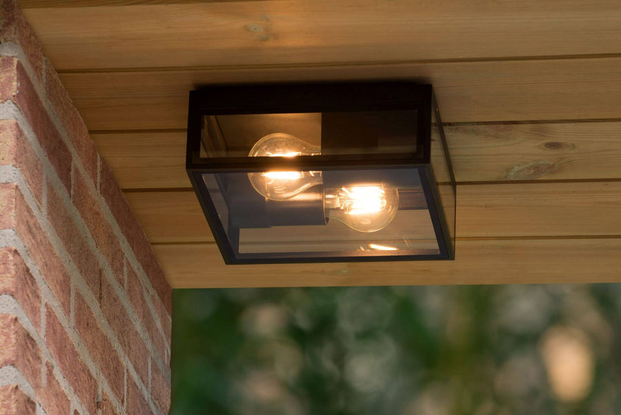 Luminaire installé sous un plafond en bois, éclairant une terrasse, brique et verdure.