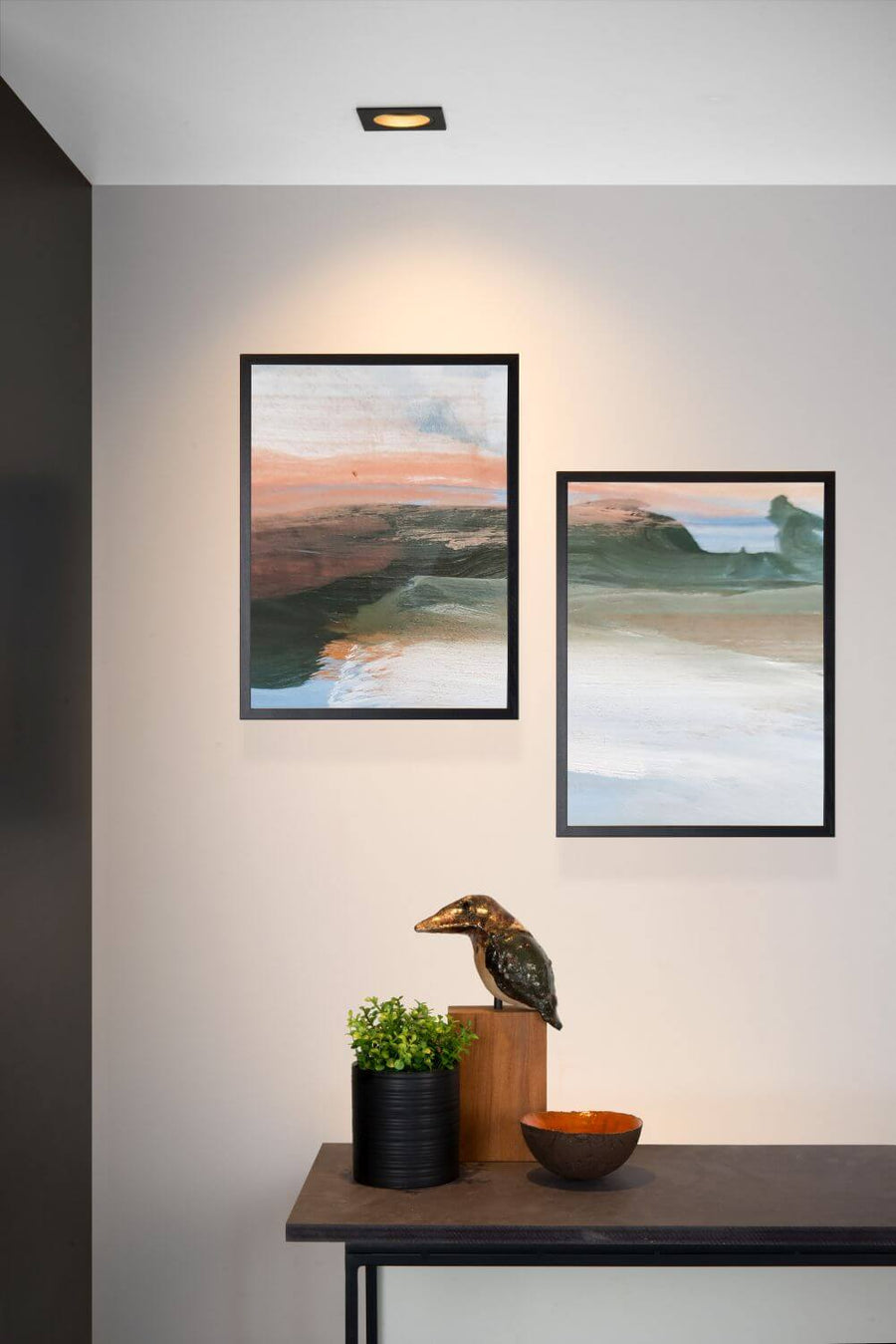 Vue rapprochée du spot encastré allumé au plafond, mettant en valeur les tableaux et objets.