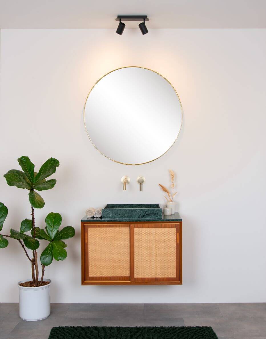 Mise en ambiance salle de bain avec plafonnier noir deux spots orientables au-dessus d'un miroir rond.