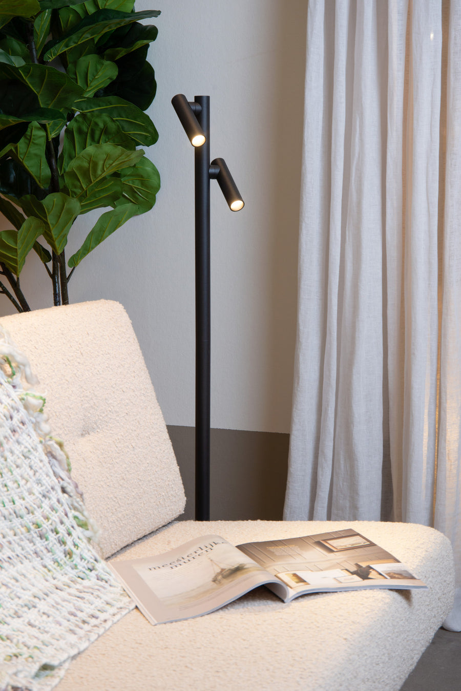 Vue rapprochée du lampadaire noir allumé, intégré près d'un fauteuil et d'un rideau.