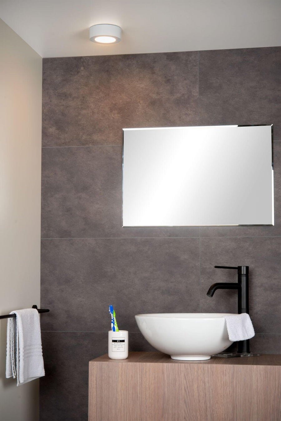 Vue rapprochée du luminaire rond fixé au plafond sur carrelage mural gris