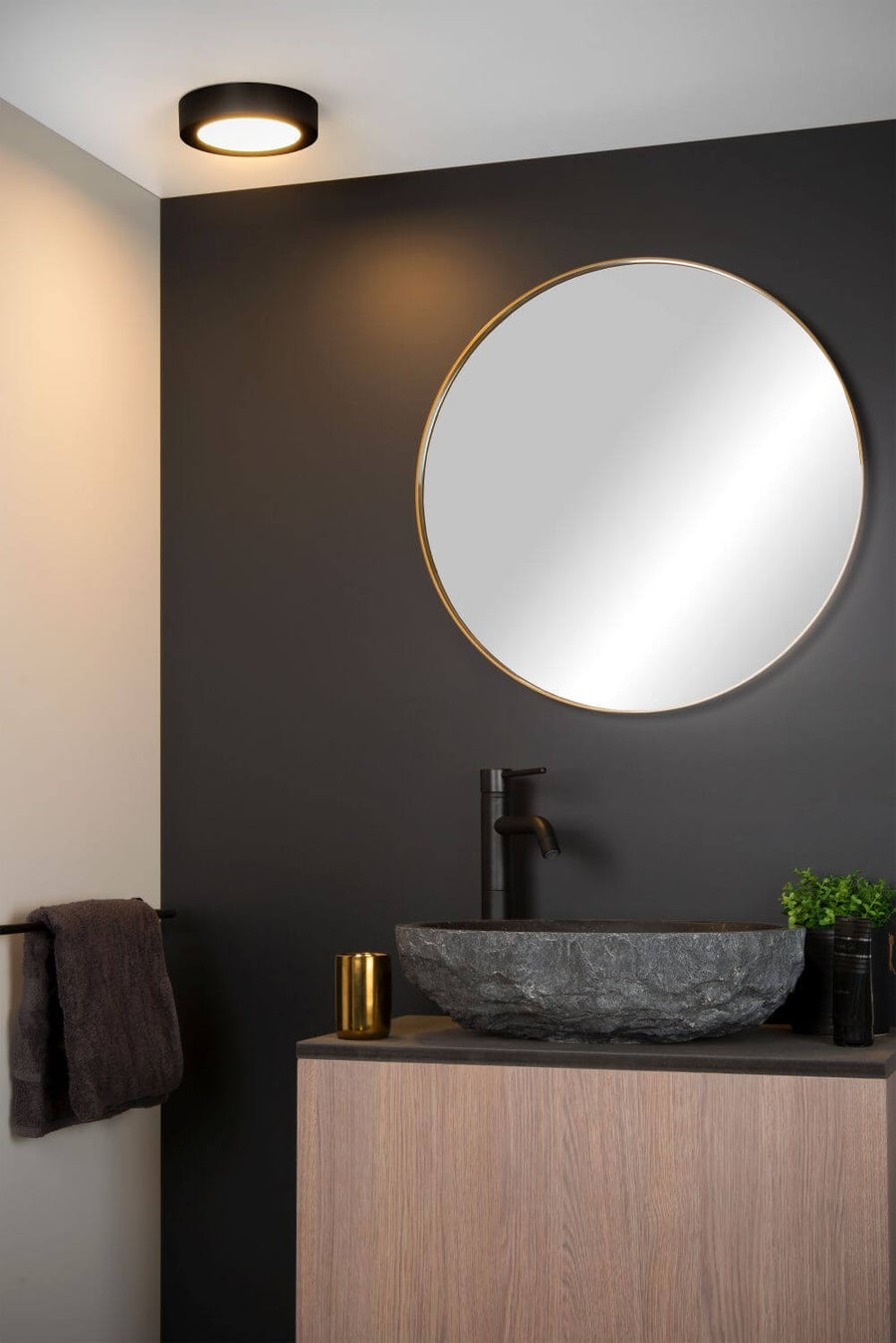 Plafonnier noir installé au plafond, éclairant une vasque en pierre et un miroir rond.