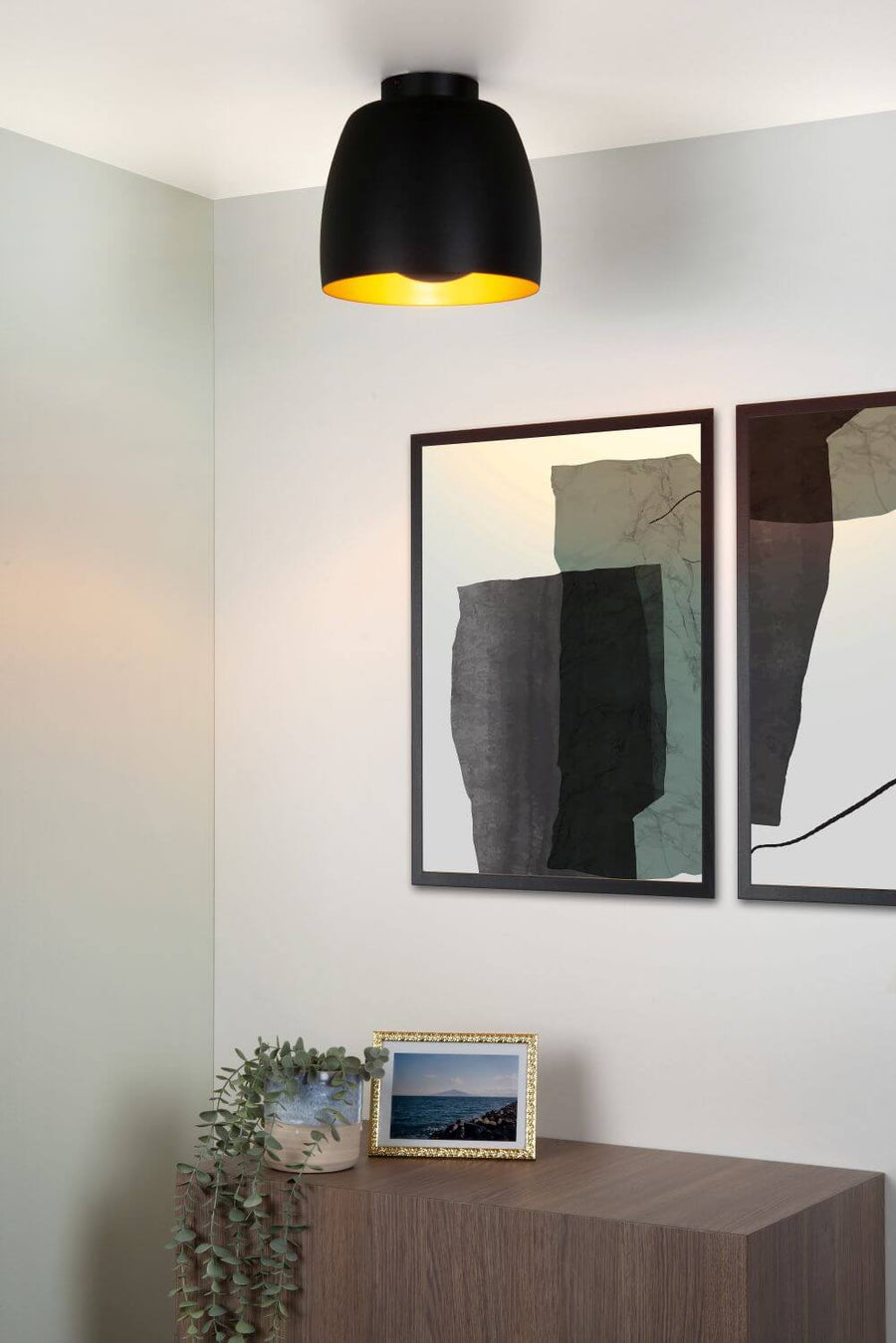 Vue rapprochée du plafonnier allumé au-dessus d’un meuble et d’affiches encadrées.