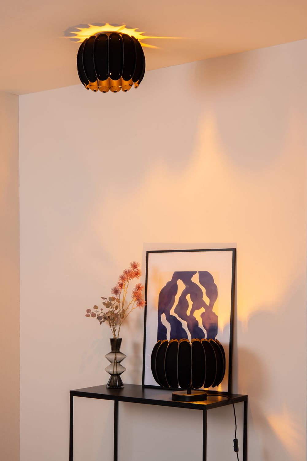 Mise en ambiance sur console noire, luminaire posé près d'un vase et d'un cadre