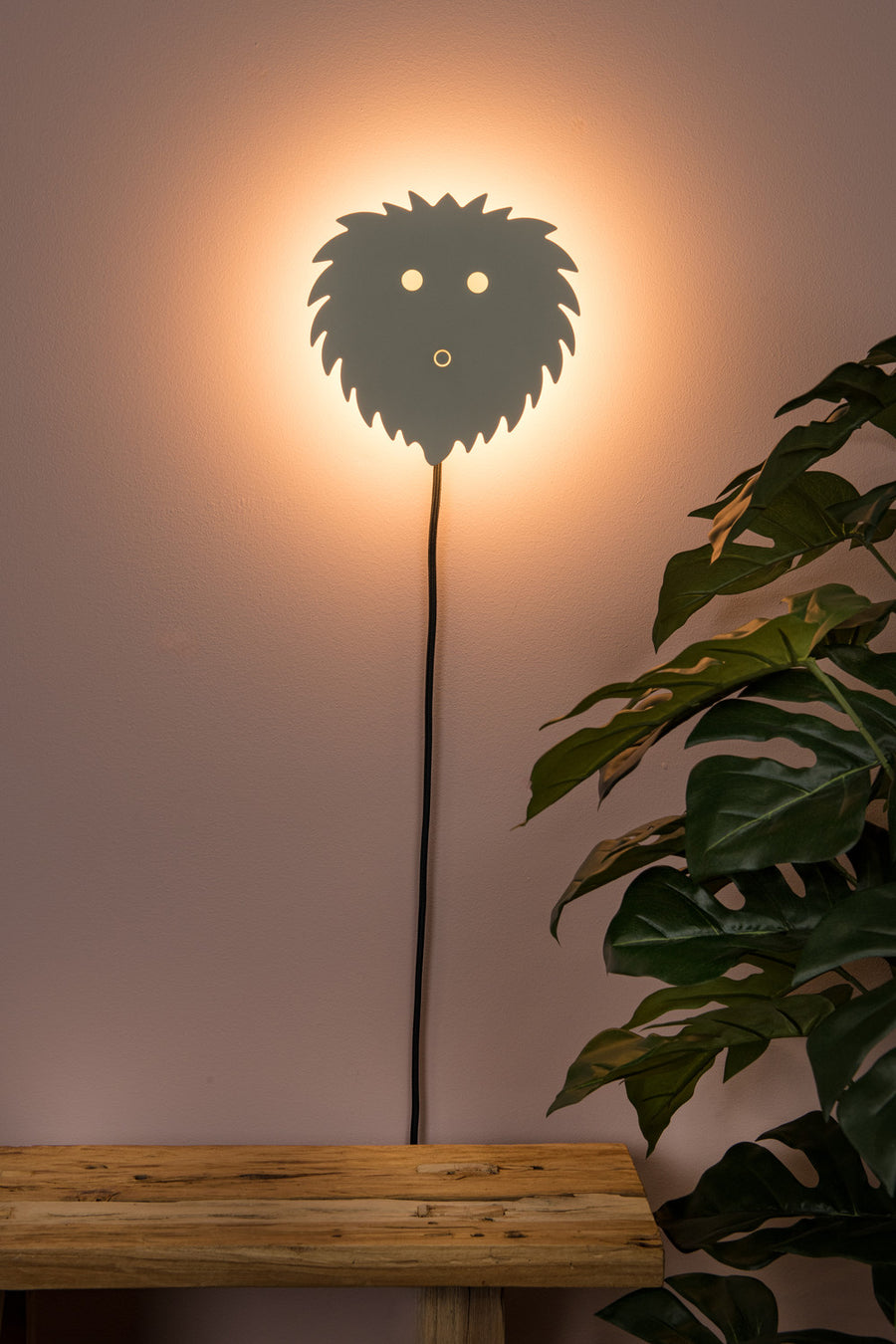 Vue de face du luminaire mural beige allumé, câble noir, table en bois