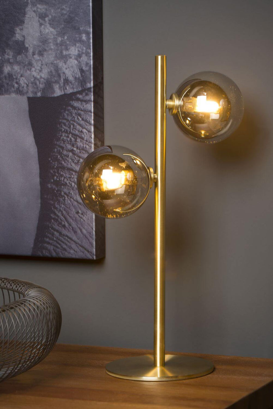 Vue rapprochée de la lampe allumée, deux globes fumés et pied doré.