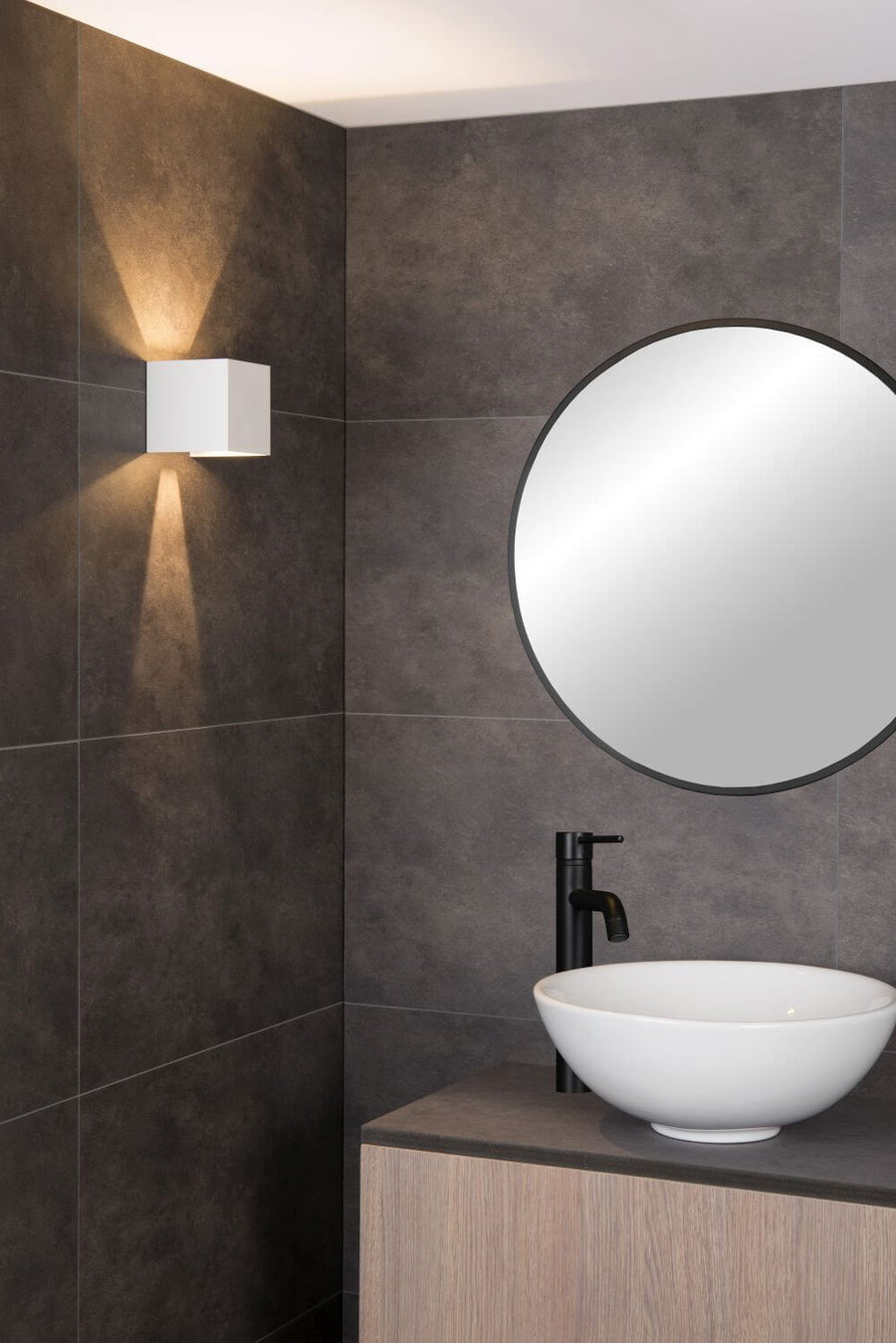 Gros plan sur l'applique murale blanche cubique, éclairant un mur de salle de bain carrelé.