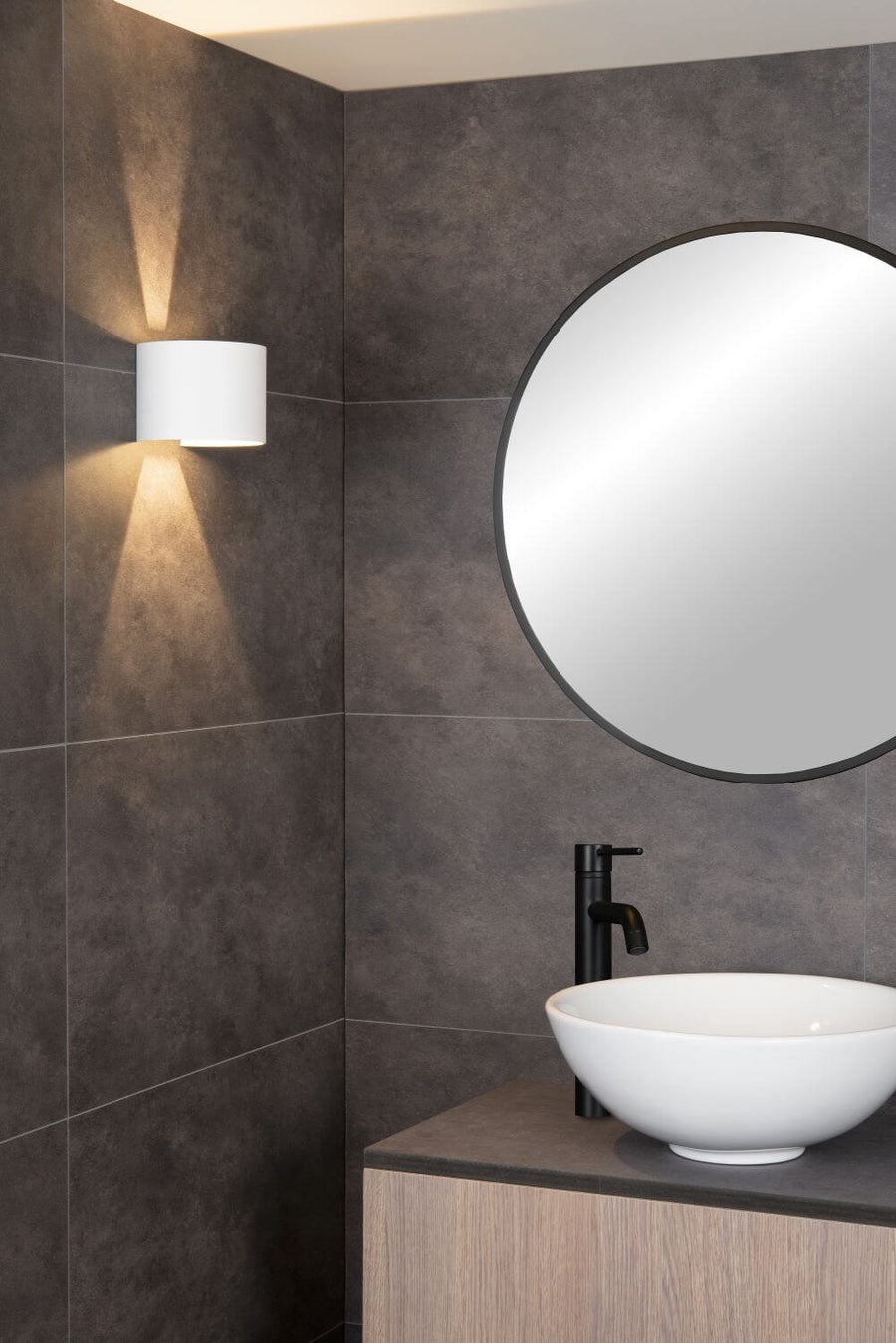 Plan rapproché de l'applique murale blanche éclairant un mur carrelé gris