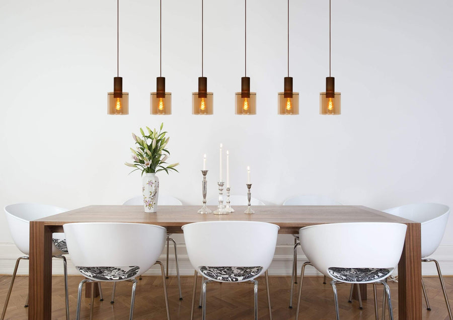 Plan large montrant une suspension aux multiples verres ambrés éclairant une table dressée de fleurs.