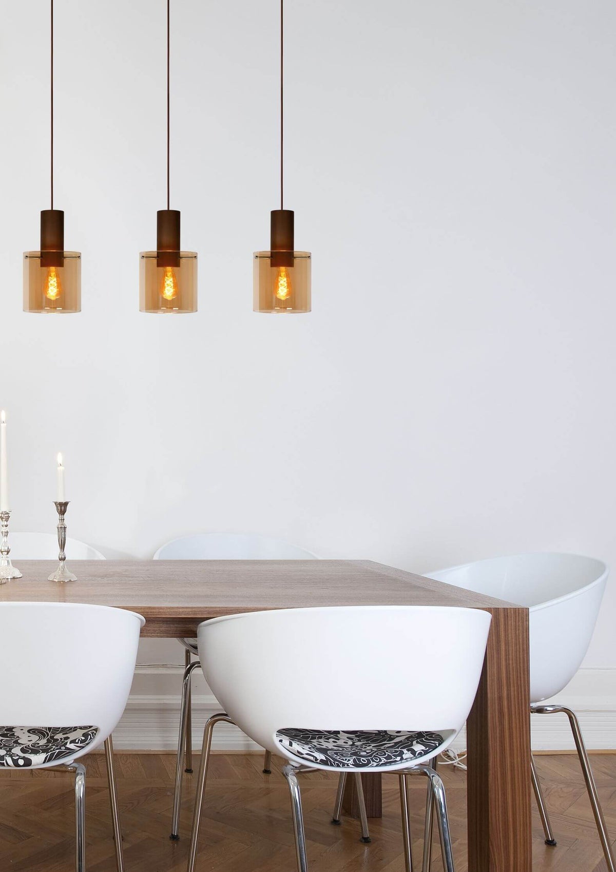 Mise en ambiance : trois suspensions en verre ambré au-dessus d'une table entourée de chaises blanches.