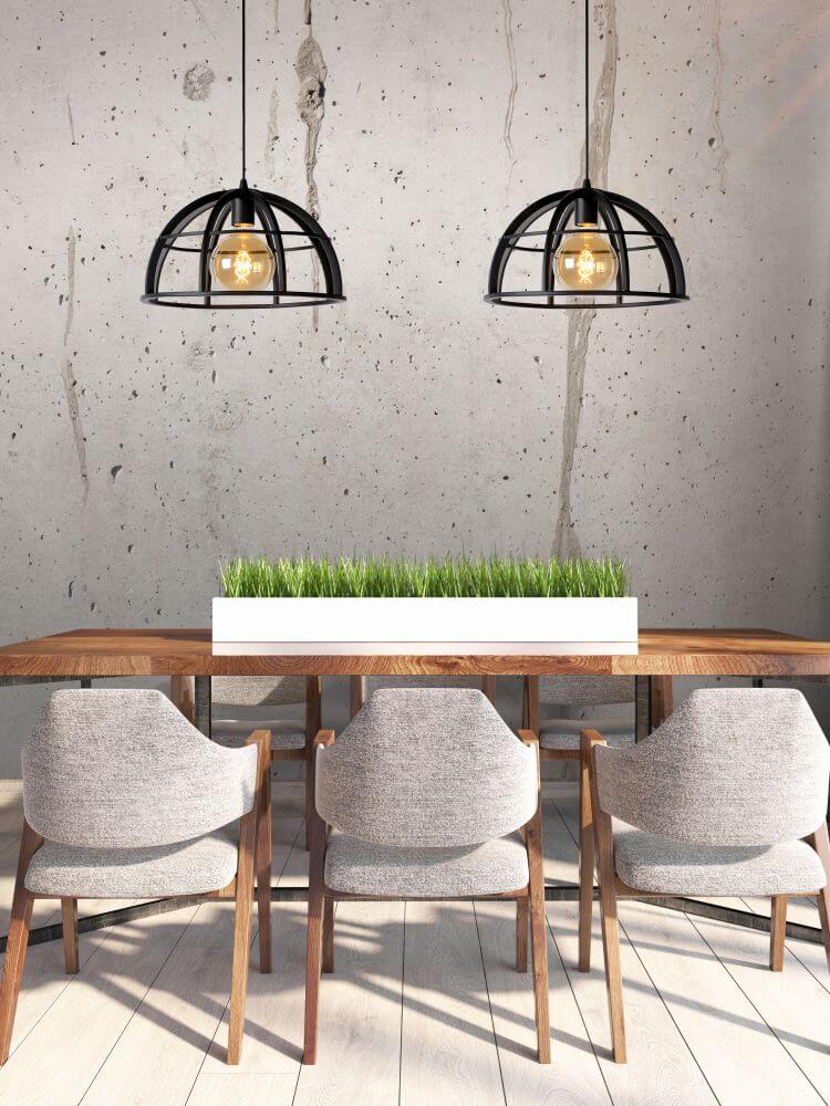 Deux suspensions noires en cage suspendues au-dessus d'une table en bois, mur béton