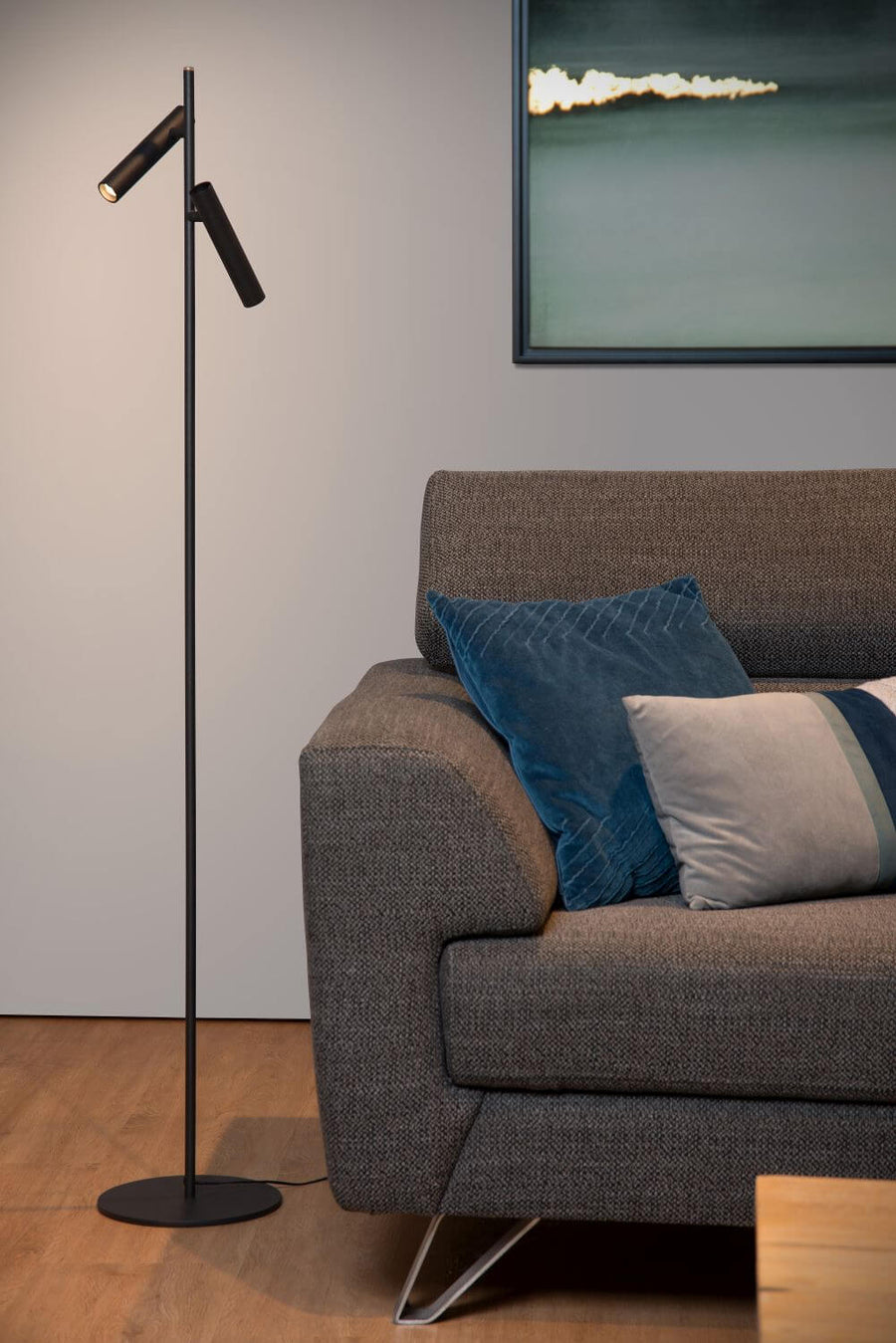 Vue de face du lampadaire noir et de ses deux spots orientables, canapé en arrière-plan