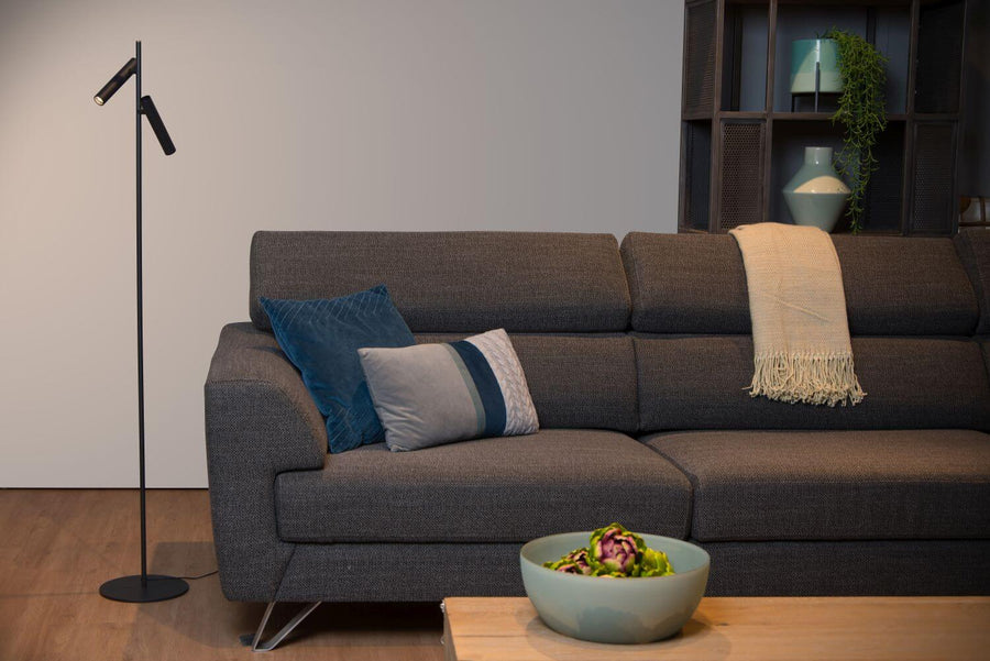 Mise en ambiance salon avec canapé, coussins, étagère et plante, lampadaire à gauche