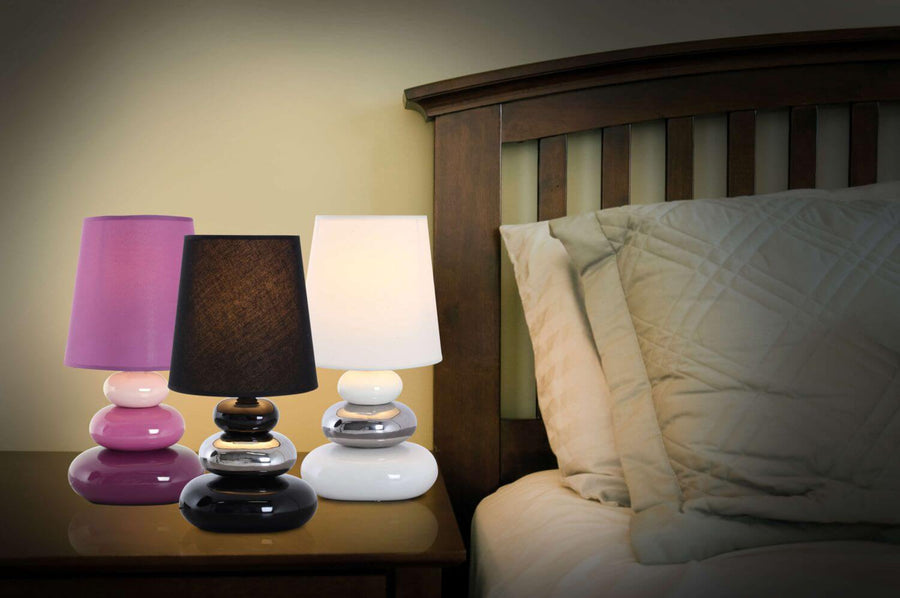 Trois lampes colorées posées sur une table de chevet en bois devant un lit