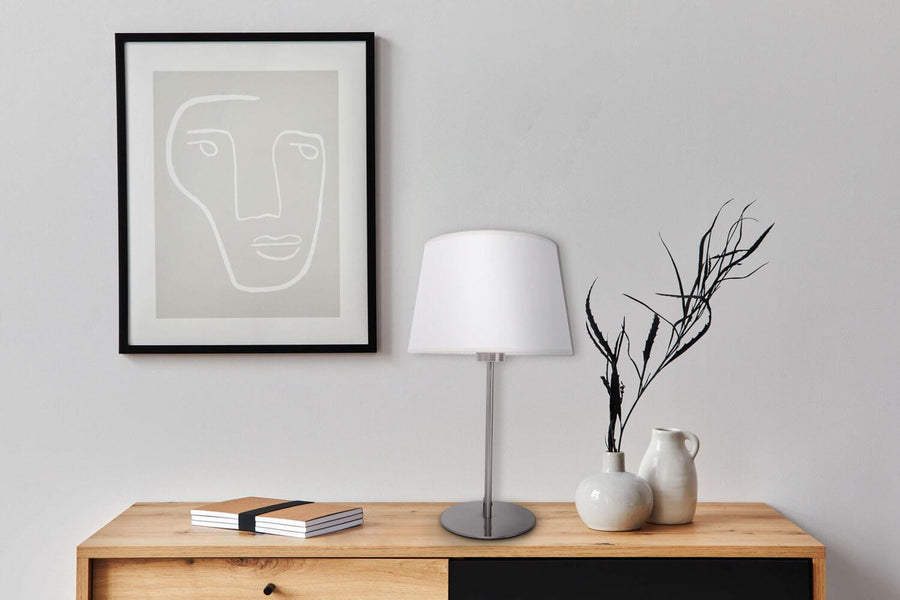 Lampe à poser beige dans un intérieur sur commode en bois avec cadre et vases