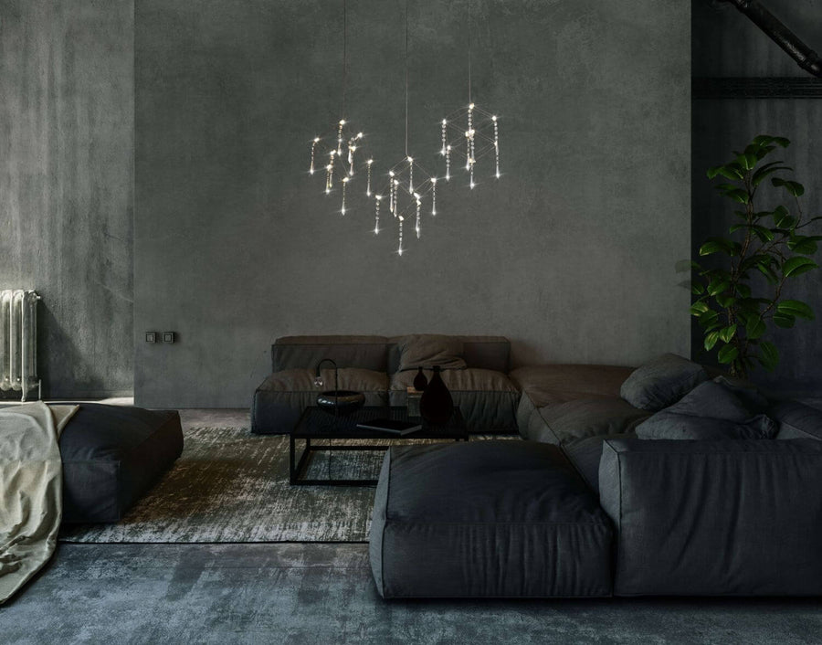 Vue rapprochée de la suspension allumée dans un salon contemporain aux canapés anthracite.