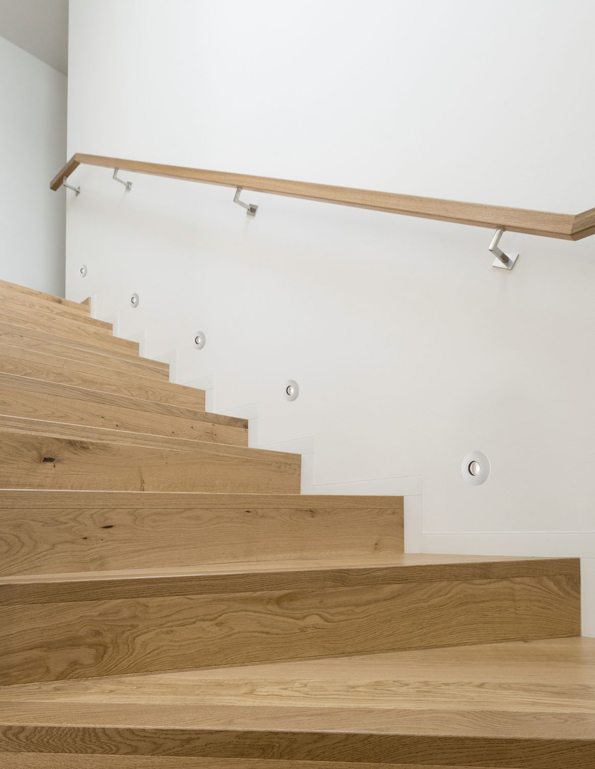Escalier intérieur en bois clair avec spots encastrés dans le mur blanc
