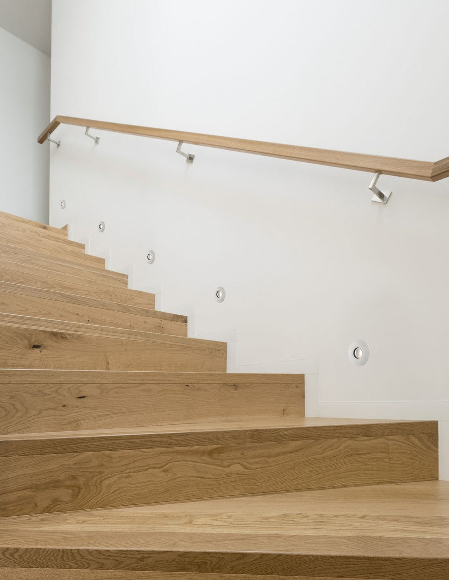 Escalier intérieur en bois clair avec spots encastrés dans le mur blanc