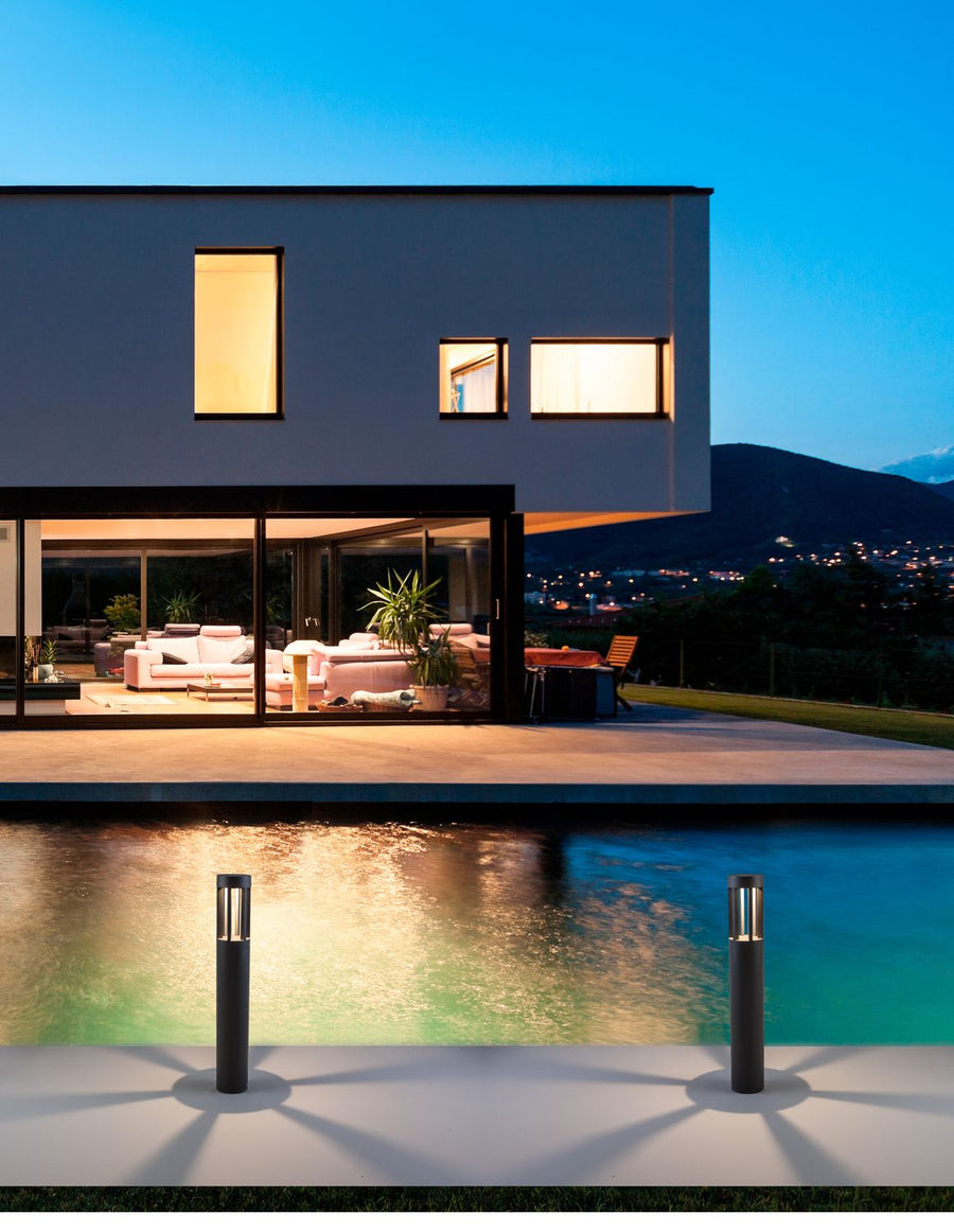 Deux bornes cylindriques éclairant la terrasse d'une villa moderne en bord de piscine au crépuscule