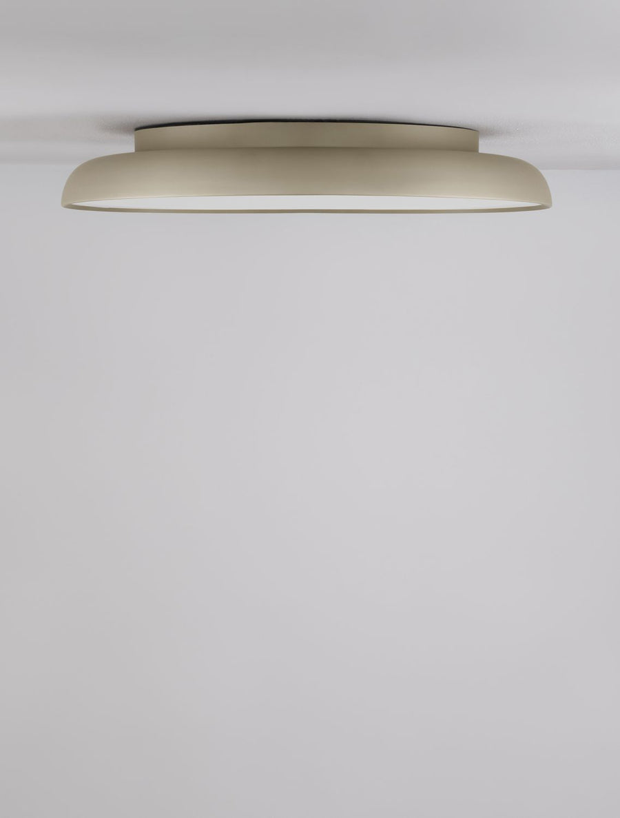 Le luminaire doré éclairé au plafond, cadrage large sur le mur blanc