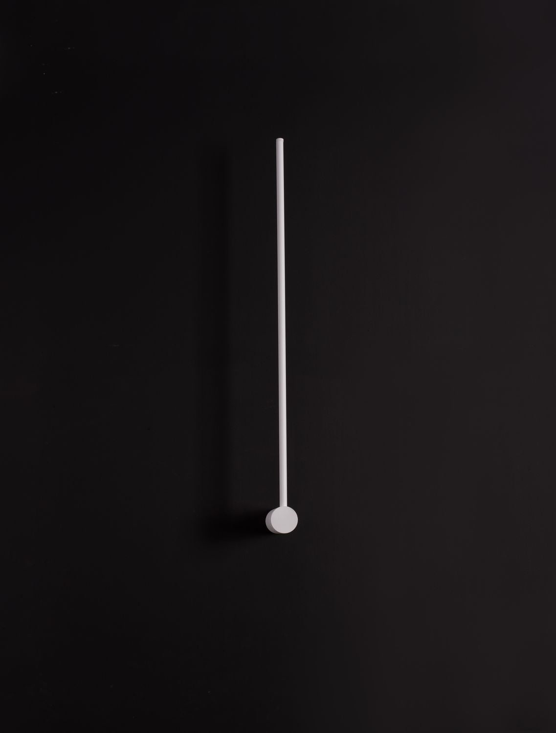 Luminaire éteint photographié sur fond noir, longue tige verticale fine