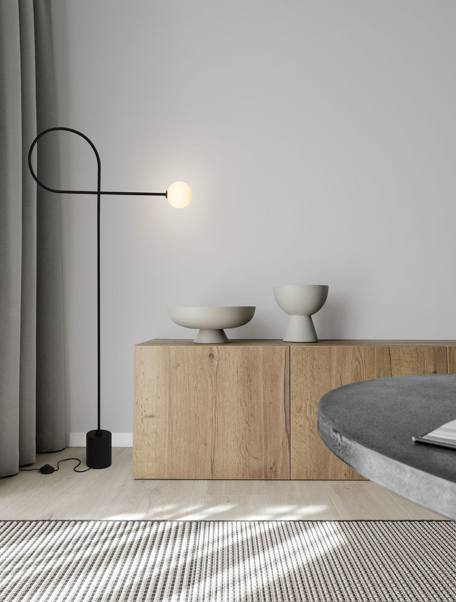 Lampadaire noir posé au sol devant un meuble en bois clair, globe allumé