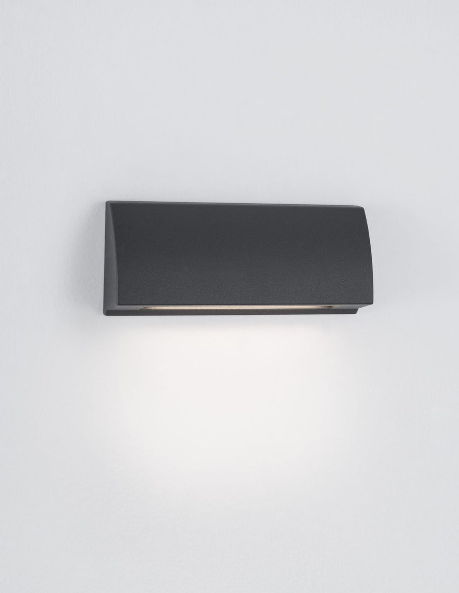 Luminaire allumé diffusant un halo de lumière vers le bas sur le mur.