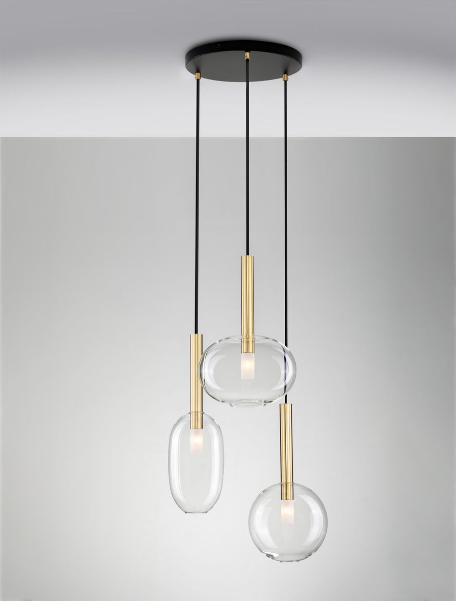 Trois suspensions allumées sur fond gris, diffusant une lumière chaude dans le verre