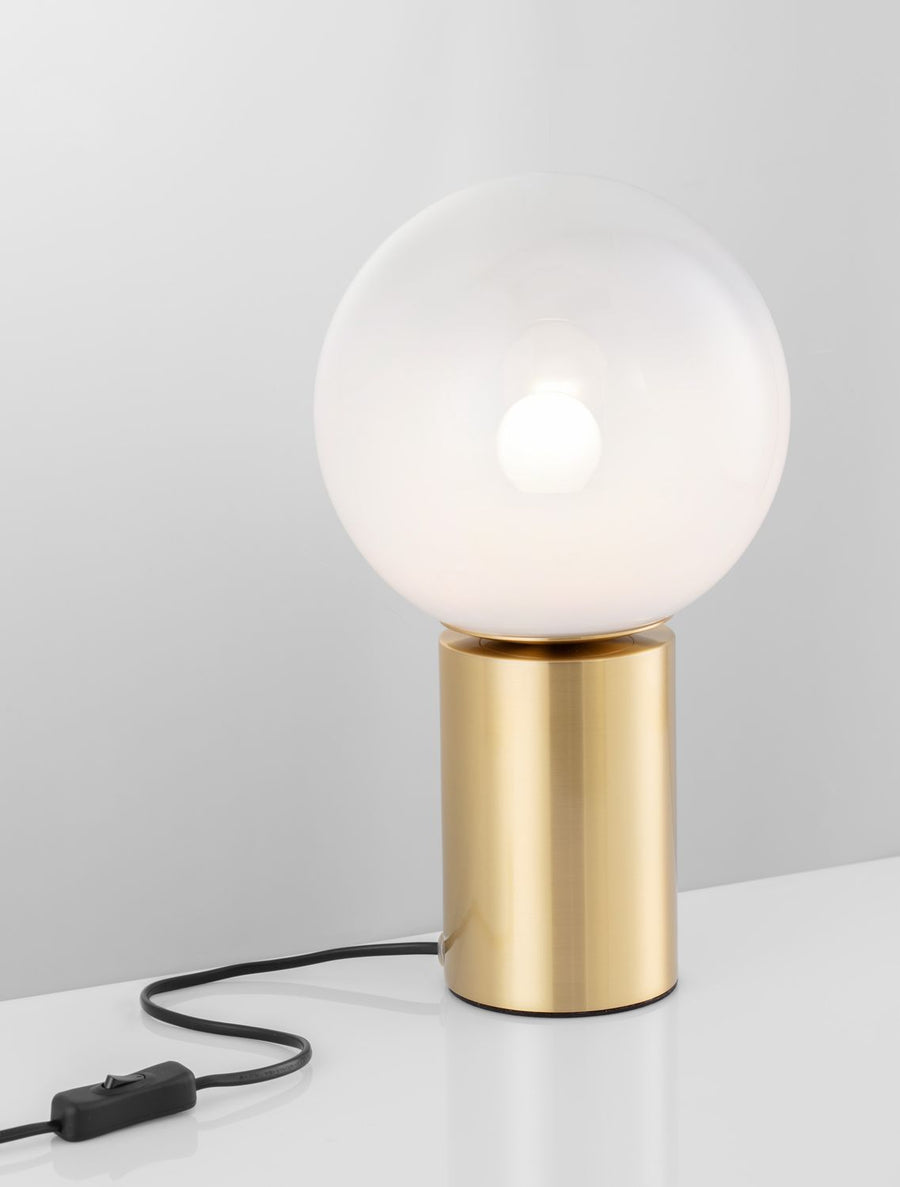 Lampe allumée, câble noir et interrupteur posés sur une surface blanche
