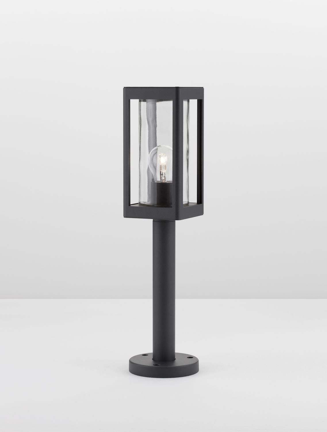 Vue du luminaire allumé sur fond blanc, ampoule visible à travers le verre transparent.