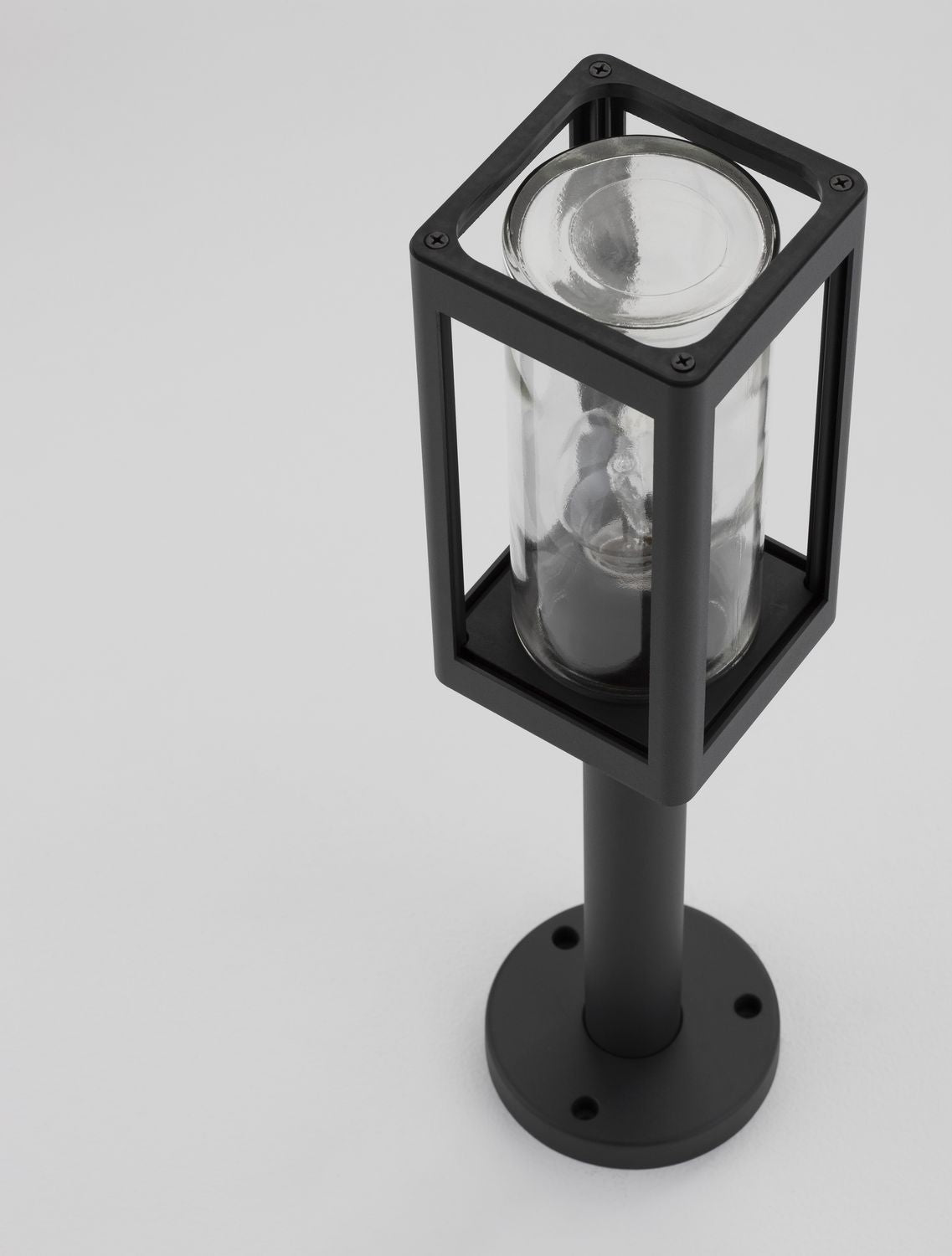 Détail du haut du luminaire, cadre noir avec vis apparentes et verre cylindrique.