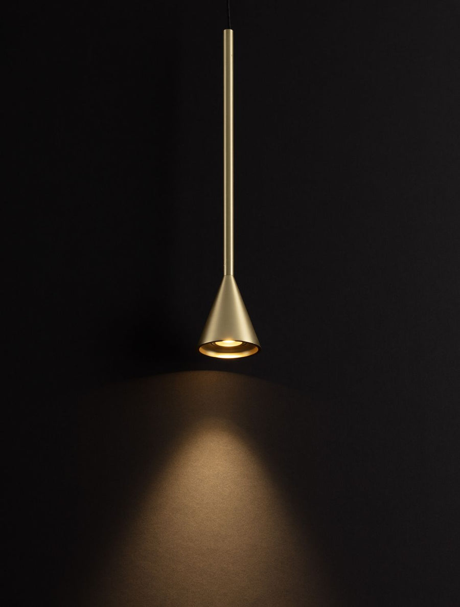 Suspension dorée allumée sur fond noir, halo de lumière chaude projeté vers le bas.