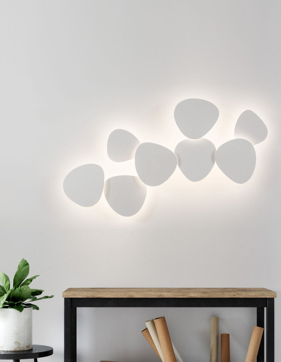 Applique murale blanche allumée au-dessus d'une console en bois et d'une plante verte