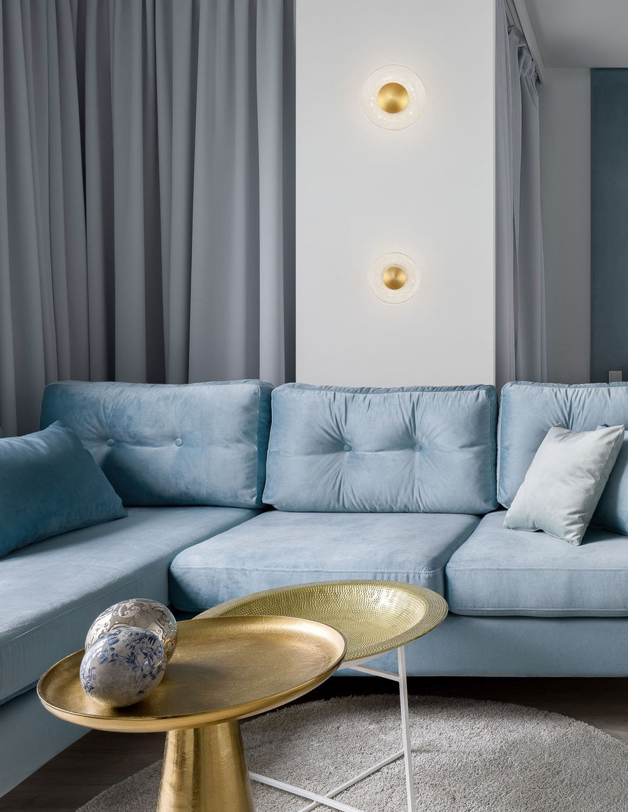 Deux appliques murales dorées éclairées au-dessus d'un canapé bleu dans un salon