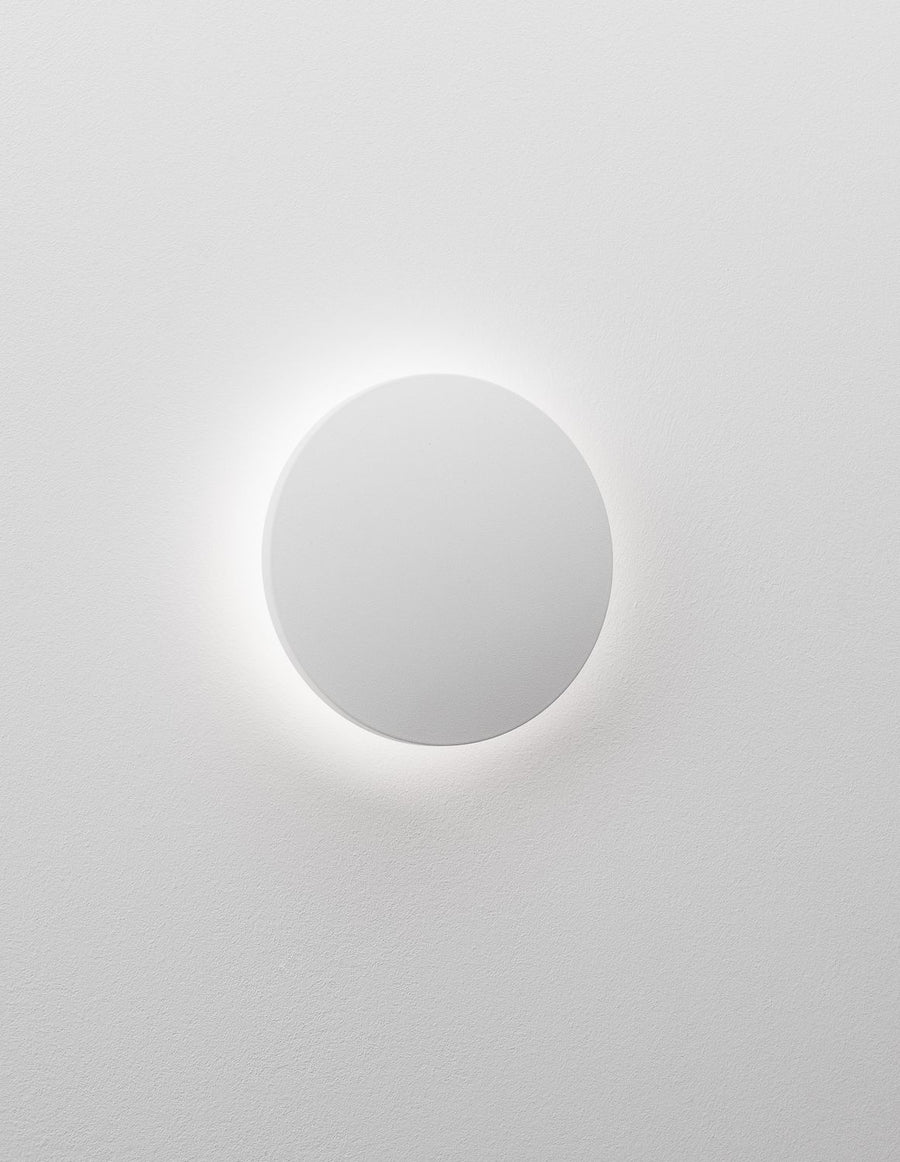 Applique ronde allumée projetant un halo lumineux diffus sur le mur
