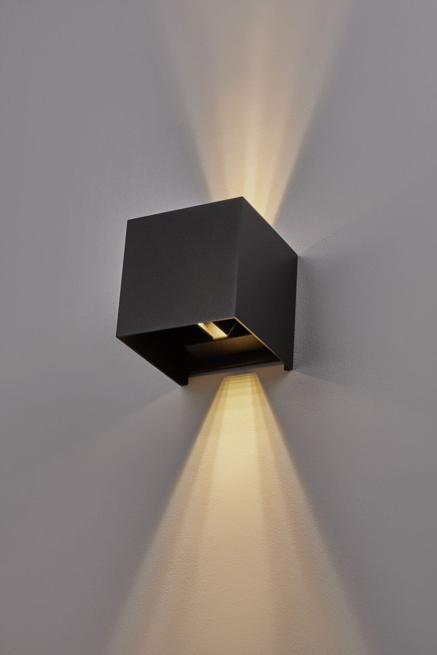 Vue rapprochée d'une applique noire allumée, avec faisceau lumineux vertical sur le mur.