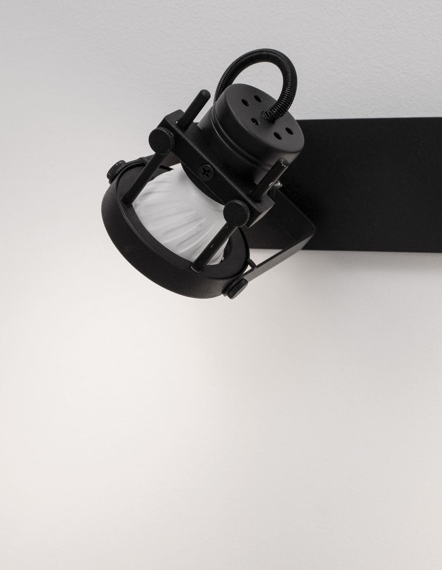 Détail rapproché d'un spot noir orientable, vis moletées et verre strié