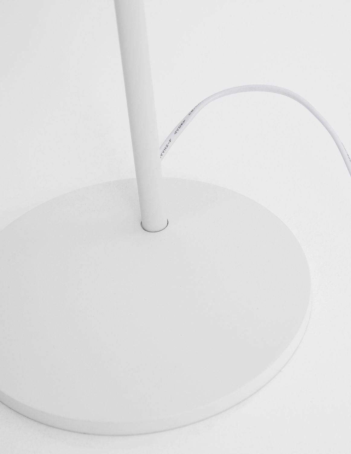 Détail de la base ronde blanche et du câble d'alimentation gainé de blanc.