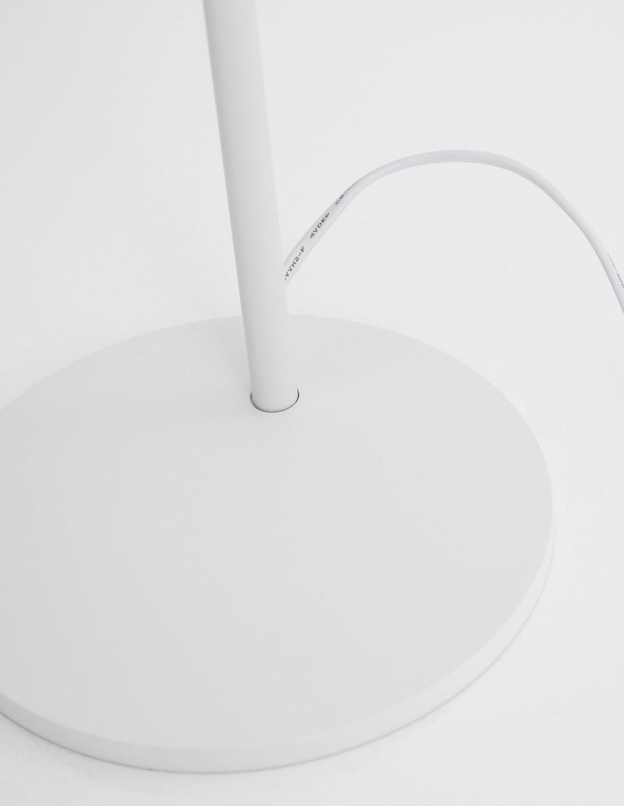 Détail de la base ronde blanche et du câble d'alimentation gainé de blanc.
