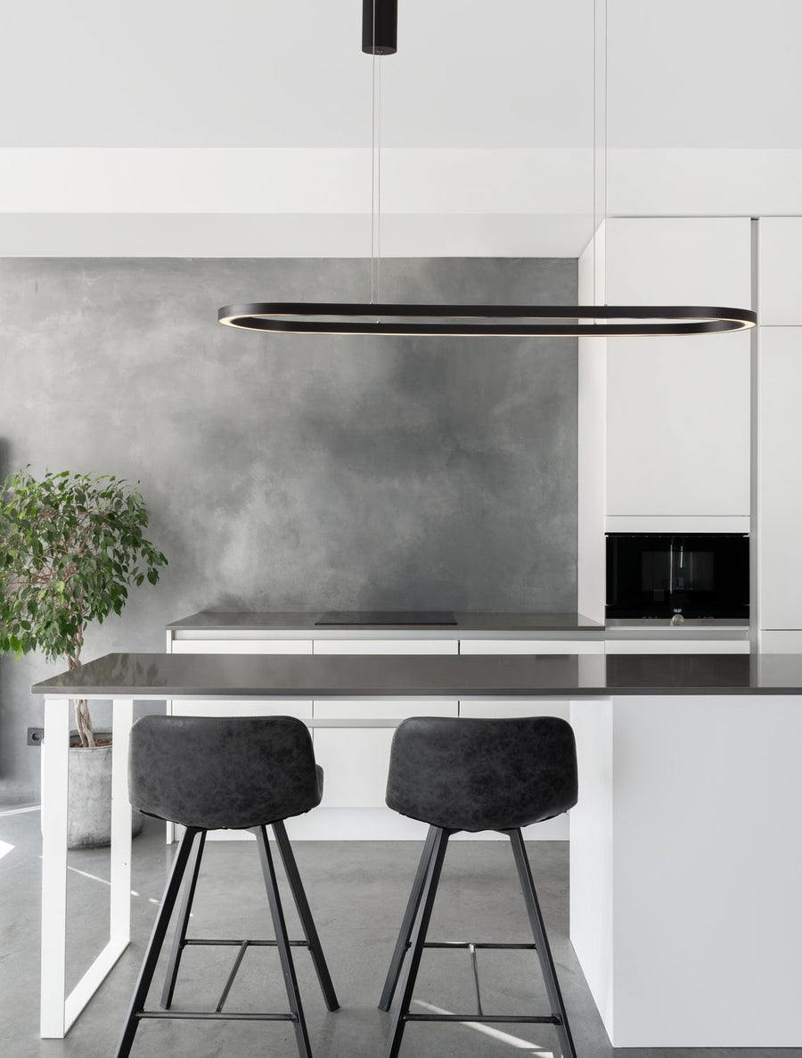Suspension noire ovale au-dessus d'un îlot de cuisine, deux tabourets et mur gris