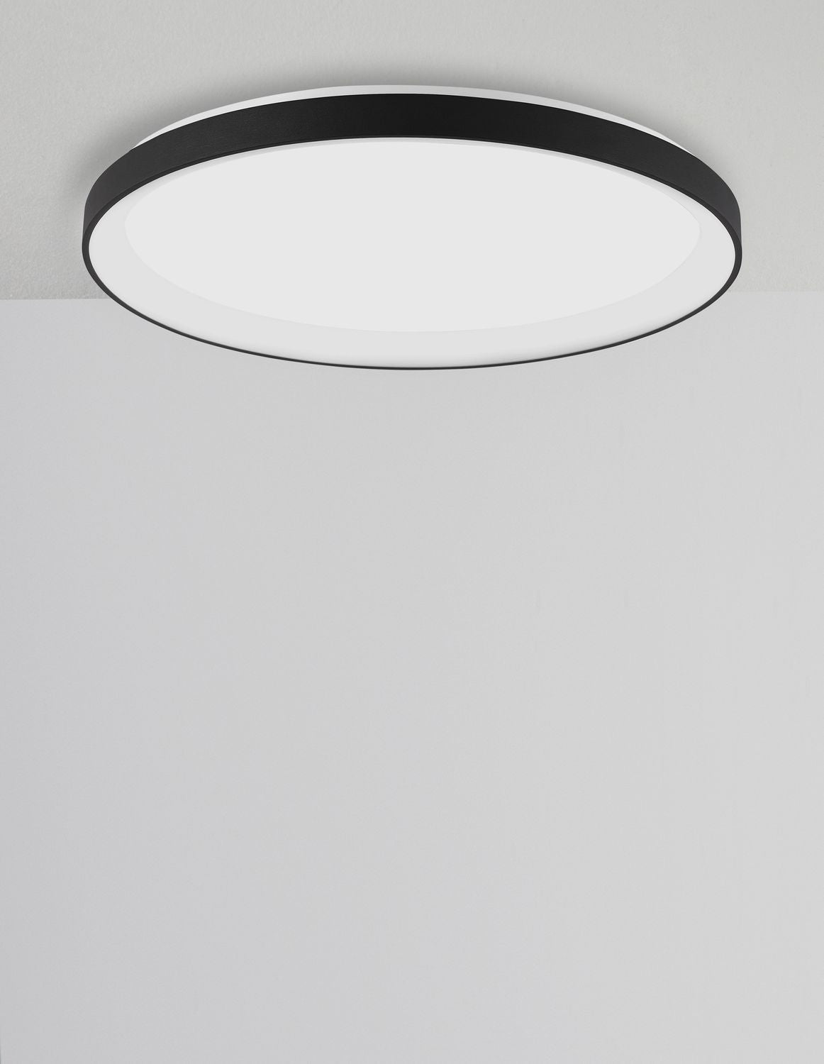 Plafonnier rond allumé, vu légèrement de biais sous un plafond gris