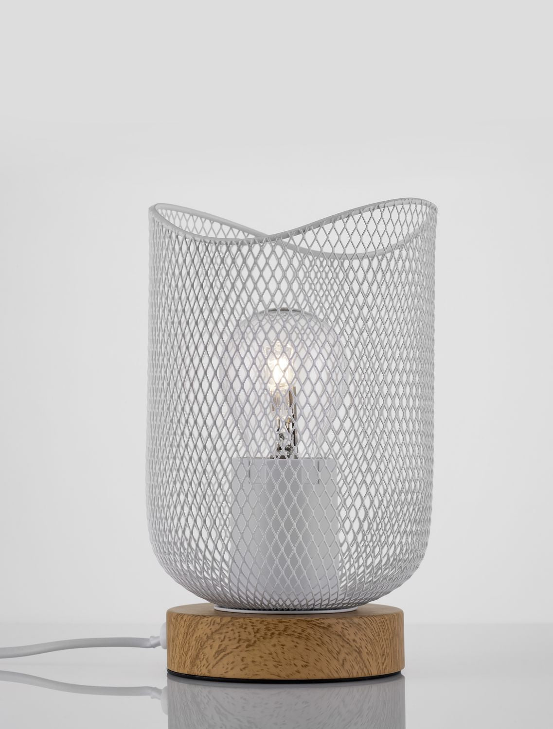 Lampe à poser en maille blanche allumée, ampoule visible à travers l'abat-jour cylindrique.